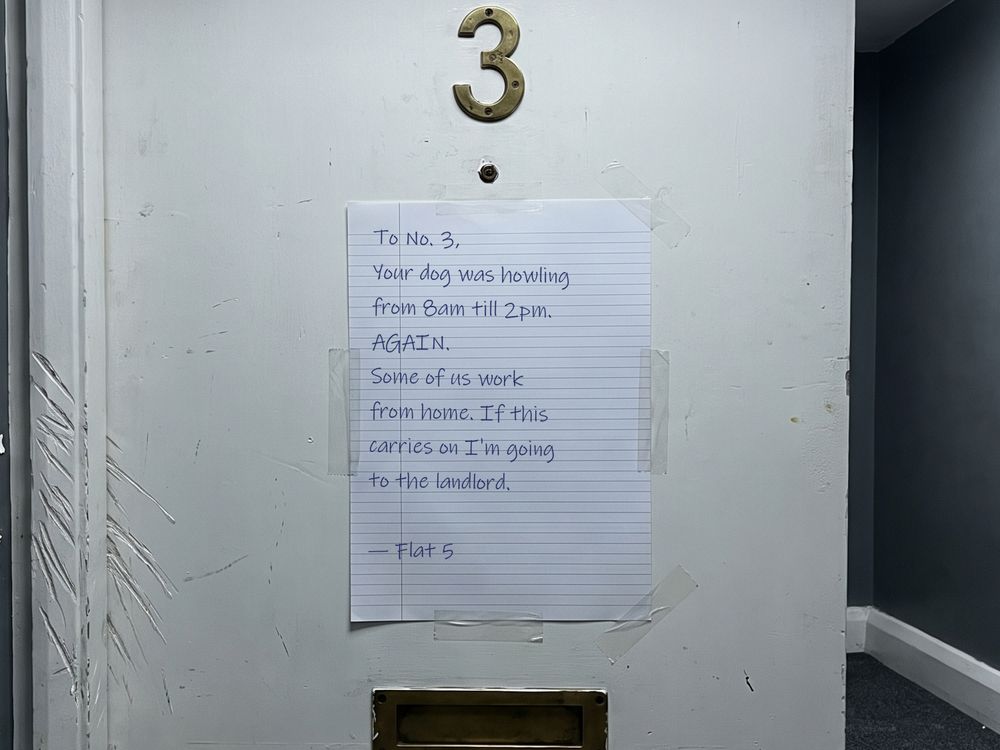 Handwritten note from a neighbour taped to a flat door complaining the dog howled from 8am till 2pm
