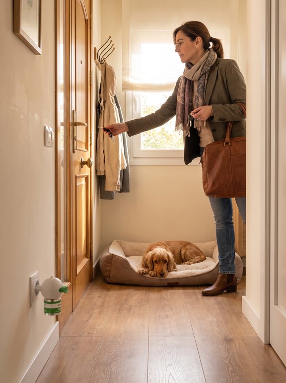 Dueña saliendo de casa mientras su perro se queda tranquilo en su cama junto al difusor Vitalys Calma
